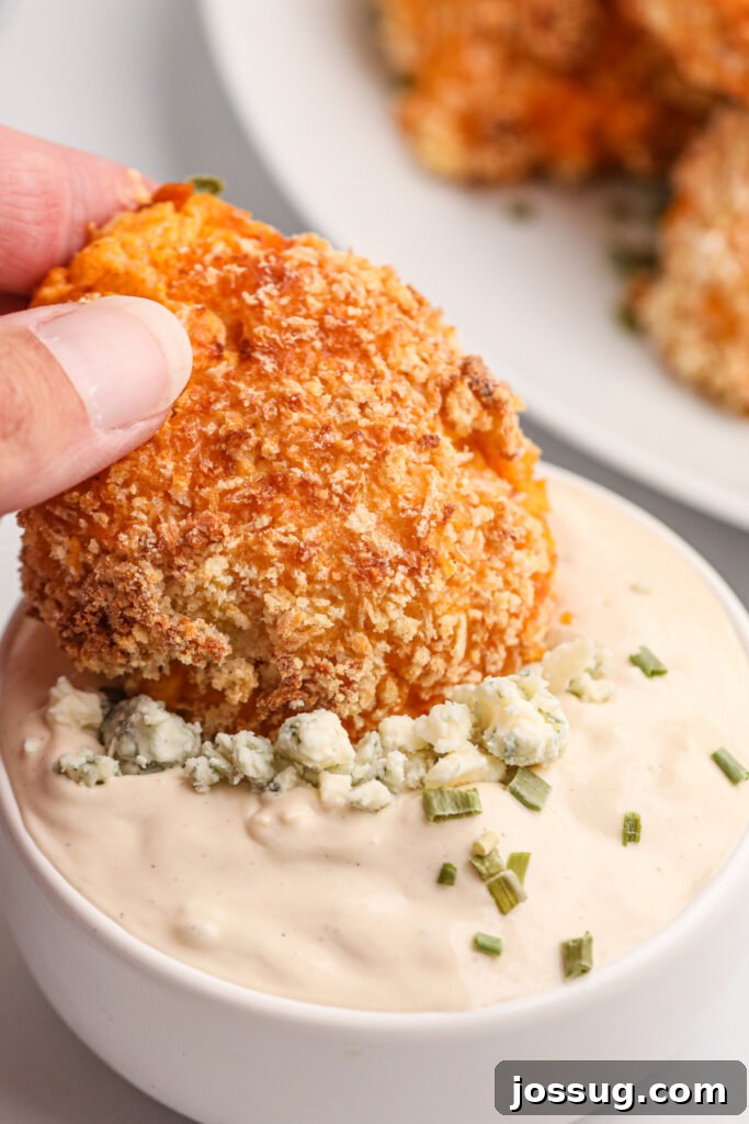 Crispy buffalo chicken popper being dipped into a creamy blue cheese dip, showcasing its golden-brown exterior and the rich texture of the dip.