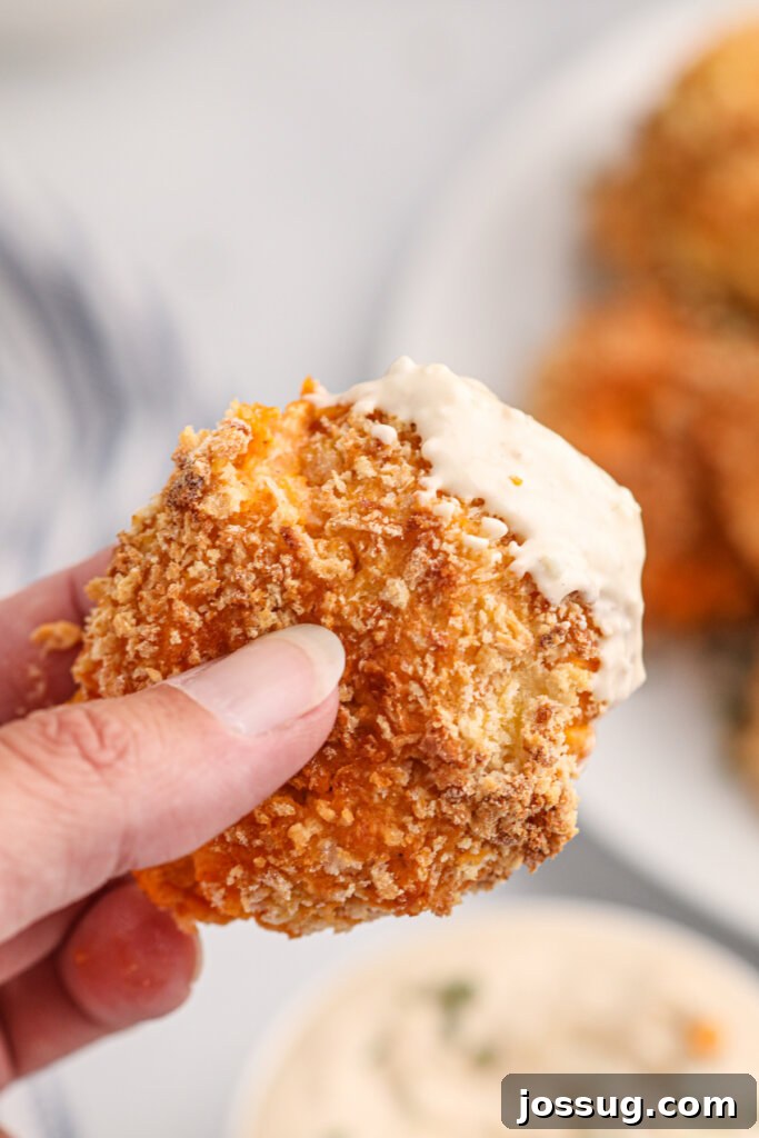 A hand holding a golden-brown air fryer buffalo chicken popper, ready to be dipped into the creamy blue cheese sauce.