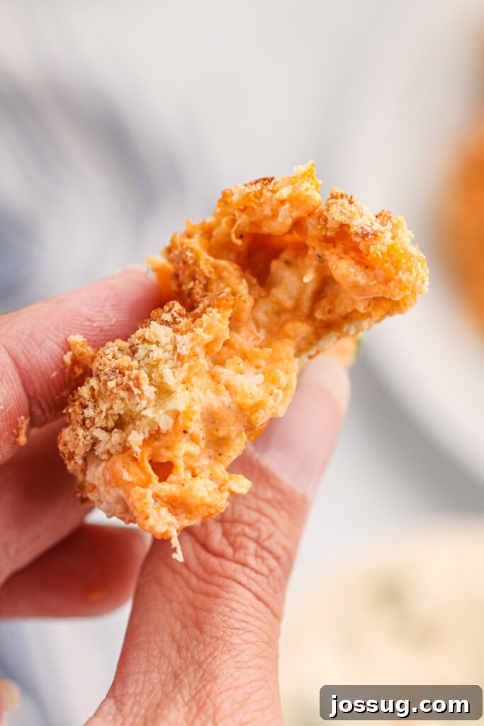 A bitten buffalo chicken popper held up, showing the cheesy, spicy buffalo chicken filling and the crispy golden exterior.