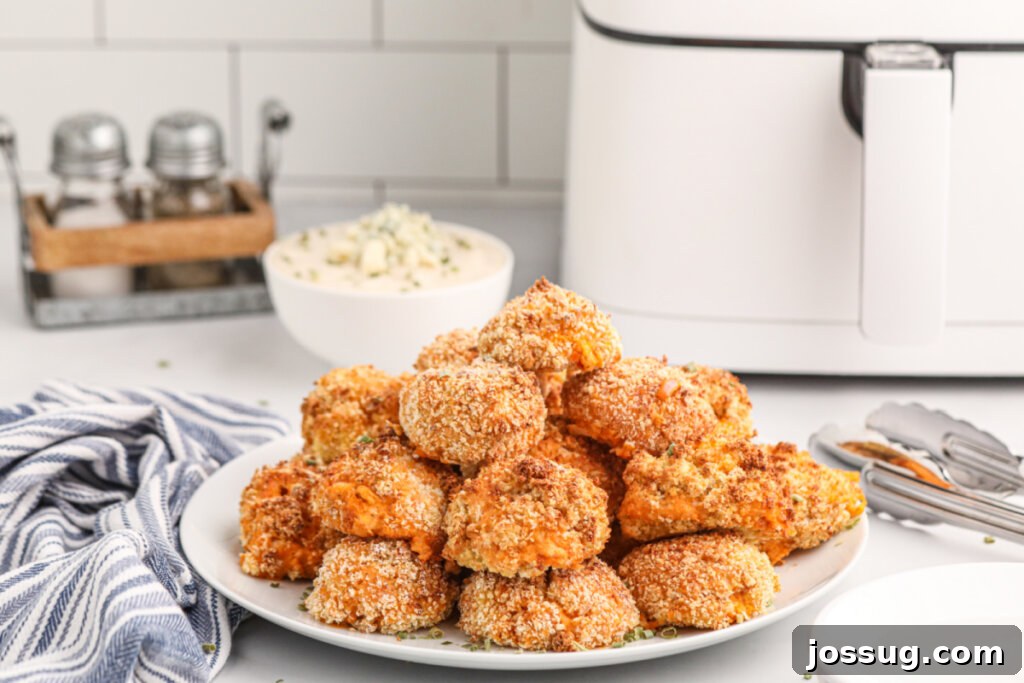 A stack of golden-brown air fryer buffalo chicken poppers arranged beautifully on a white serving plate, garnished with fresh herbs.