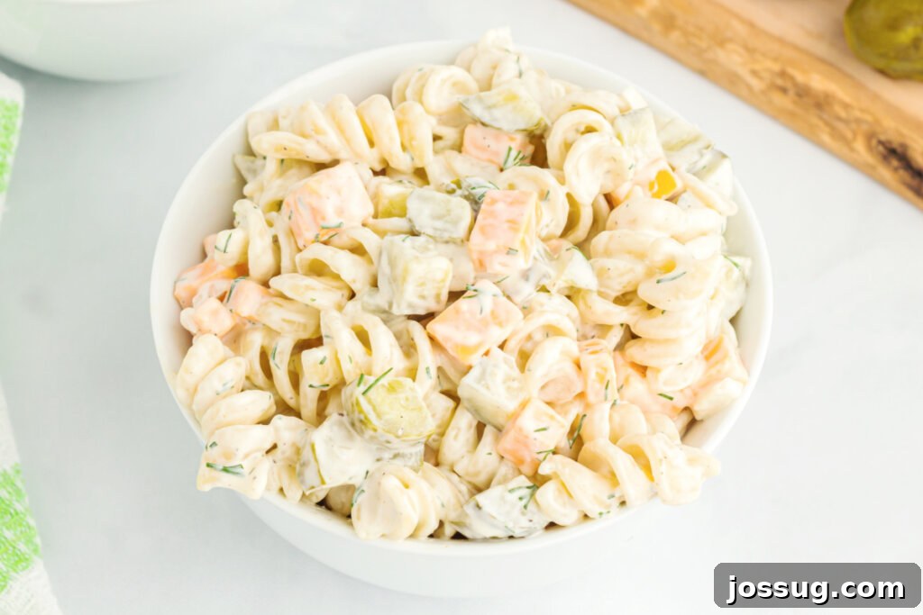 A close-up view looking down into a bowl of vibrant dill pickle pasta salad