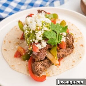 Close-up square image of a steak fajita taco with guacamole, cheese, and cilantro on a white plate.