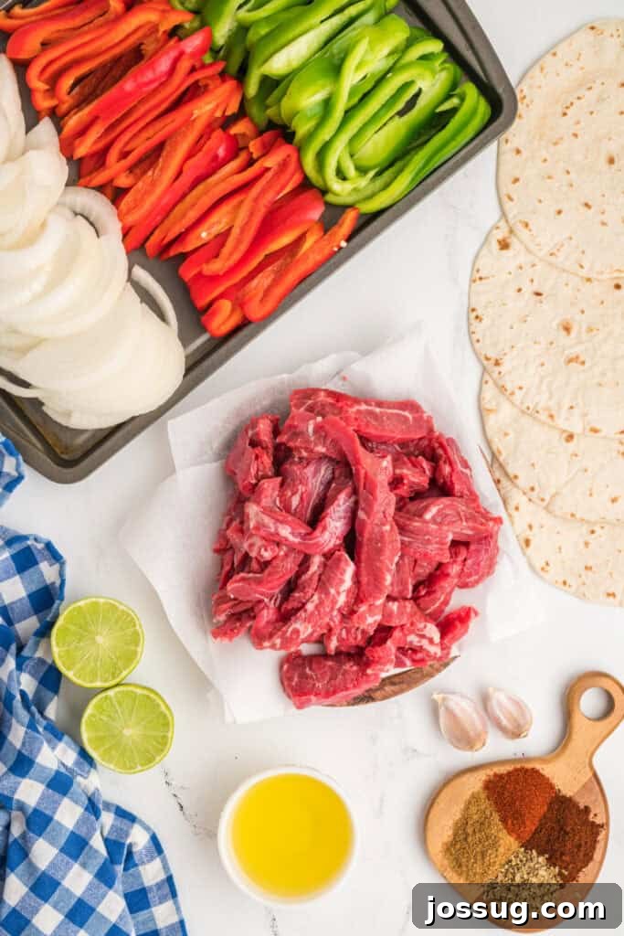 Overhead view of raw fajita ingredients including sliced peppers, onions, flank steak, lime, garlic, olive oil, and spices.