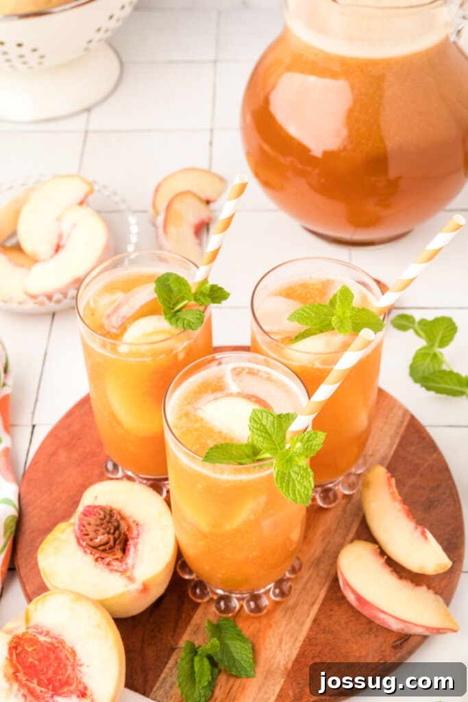 Three glasses of iced peach tea with fresh peach slices and mint sprigs, arranged on a rustic wooden serving tray, gleaming in natural light.
