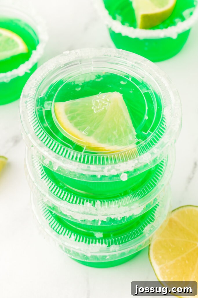 Three perfectly set lime margarita jello shots, garnished with lime wedges and salt rims, stacked for an appealing presentation.