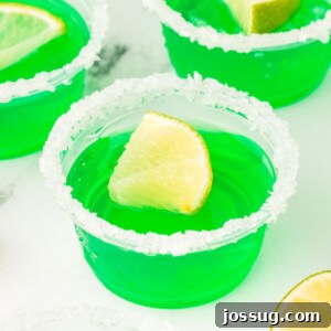 Closeup of a single, vibrant lime margarita jello shot with a salt rim and lime wedge garnish.