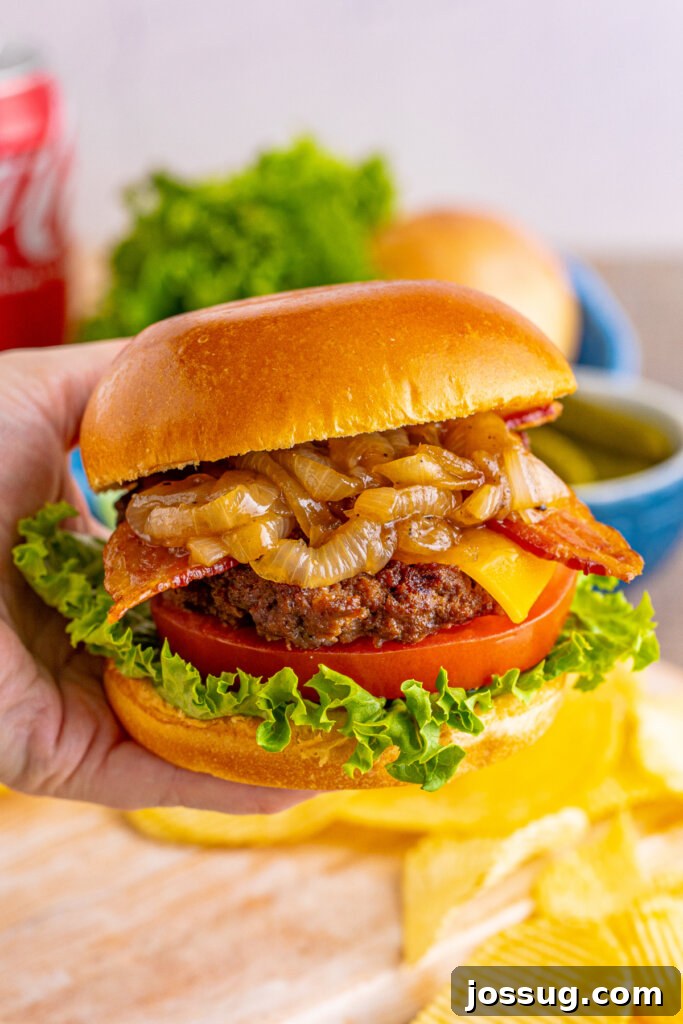 Coke-Glazed Onion Bacon Cheeseburgers 3 A hand presenting a perfectly cooked bacon cheeseburger, showcasing its layers of fresh ingredients and caramelized onions.