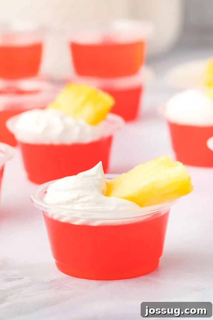 Caribbean Rum Jelly Shooters 3 A close-up of rum punch jello shots elegantly topped with whipped cream and a fresh pineapple piece, ready to be served.