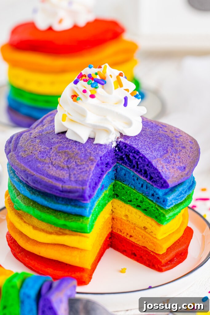 stack of rainbow pancakes with a triangle bite taken off the front to show the fluffy inside