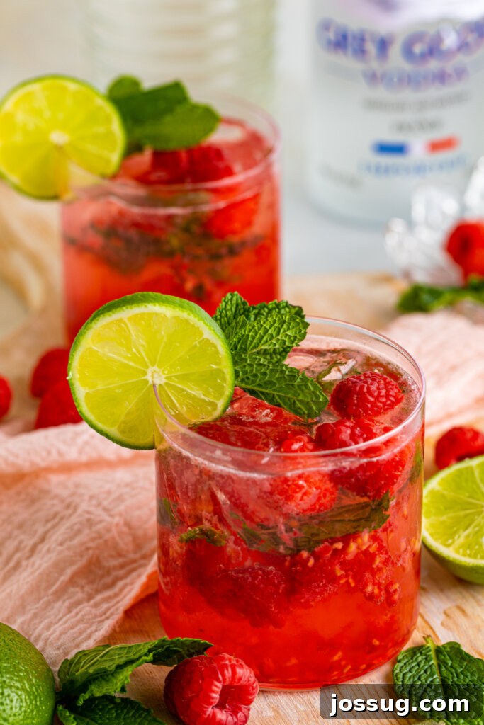 Two Berry Vodka Smash cocktails garnished with fresh berries and mint, set on a bright table.