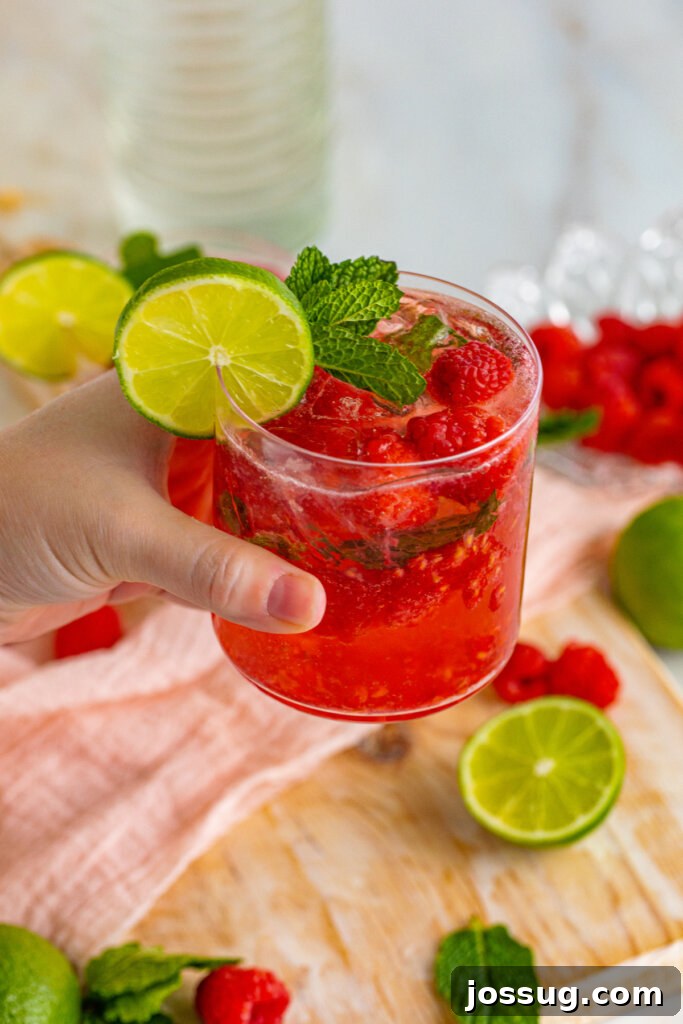 A hand holding a Berry Vodka Smash cocktail, highlighting its vibrant colors and garnishes.