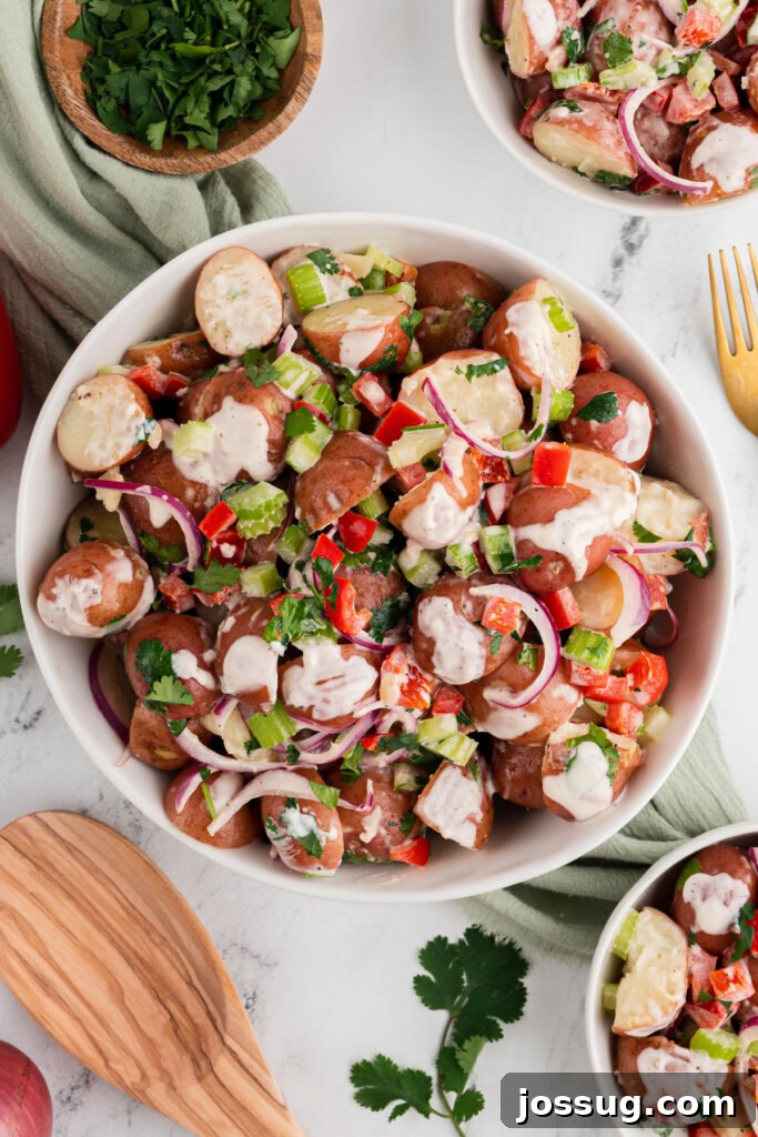 White serving bowl brimming with fresh Red Potato Salad, garnished with fresh herbs