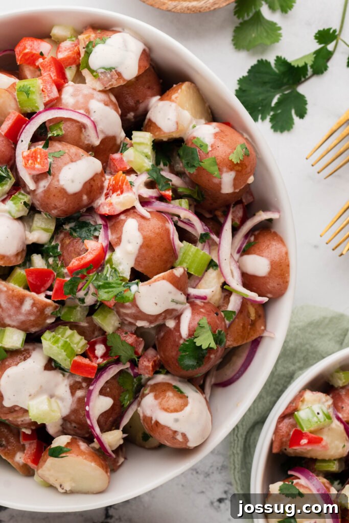 Overhead shot of a white bowl filled with Red Potato Salad, garnished with fresh herbs