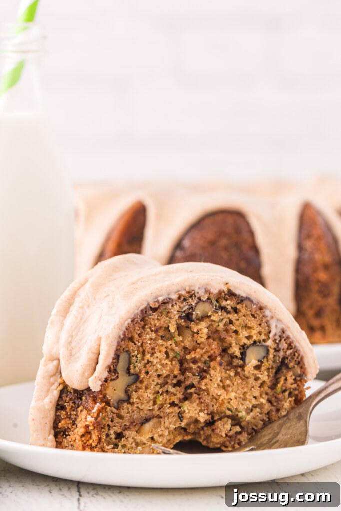 Garden Green Bundt Delight 2 A moist slice of homemade Zucchini Bundt Cake with cinnamon icing on a white plate, with the full cake visible in the background.