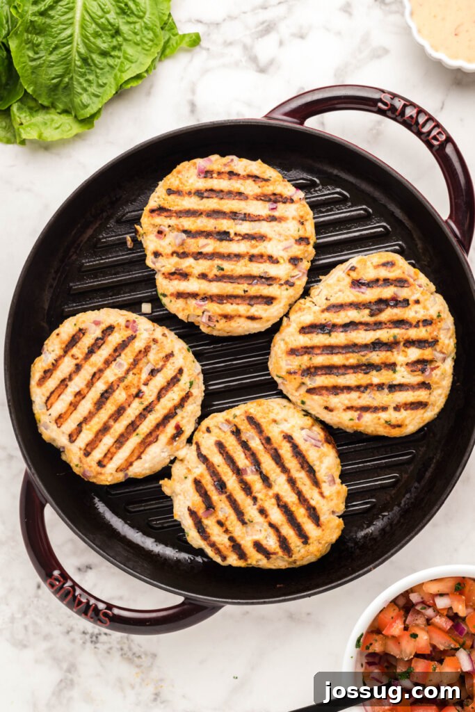 Explosive Bang-Bang Chicken Burgers 4 Chicken patties sizzling on a grill pan, forming beautiful grill marks.