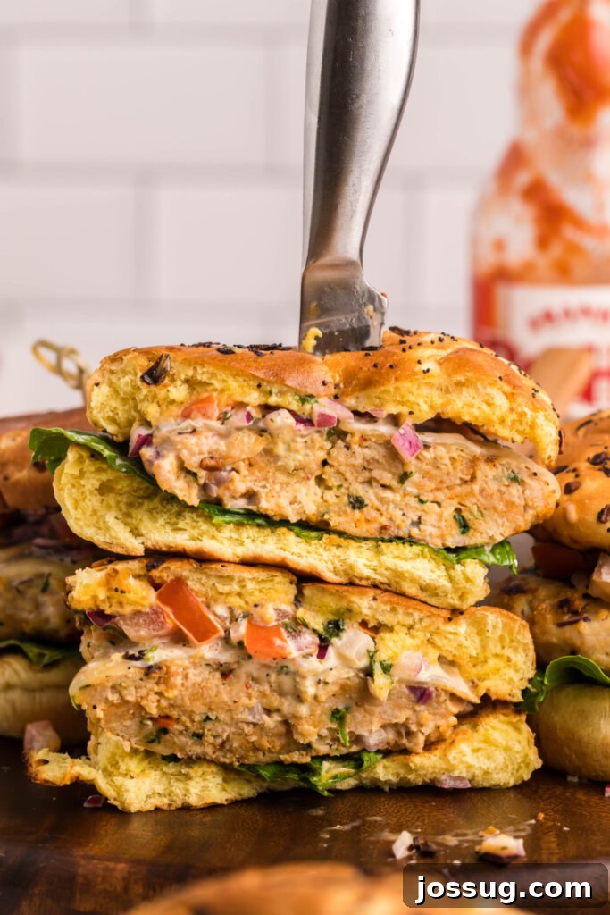 Explosive Bang-Bang Chicken Burgers 6 A freshly prepared chicken burger with Bang-Bang sauce, sliced in half and stacked, with a knife stabbed through, presented on a cutting board.