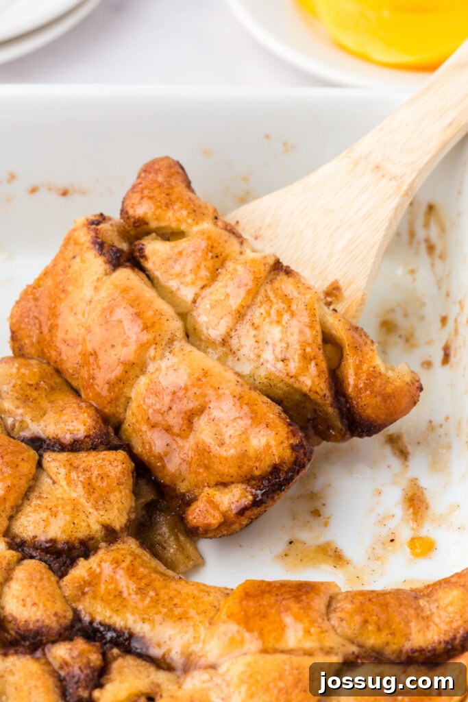 Two warm Peach Crescent Dumplings being carefully scooped out of the baking pan with a serving utensil, highlighting their golden crust and juicy filling.