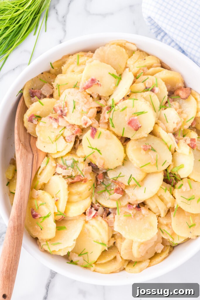 Classic German Potato Salad in a white serving bowl, garnished with fresh chives, ready to be enjoyed at a picnic or gathering.