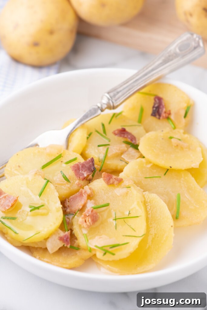A portion of warm German potato salad on a small white plate, served as a side dish, garnished with fresh herbs.