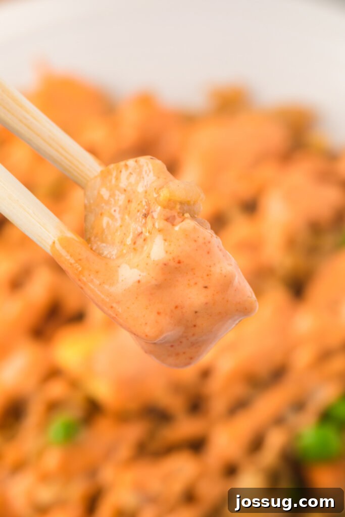 Irresistible Dipping Sauce 3 Chopsticks holding a piece of cooked chicken drizzled generously with homemade Yum Yum Sauce, highlighting its rich texture and appetizing appeal.