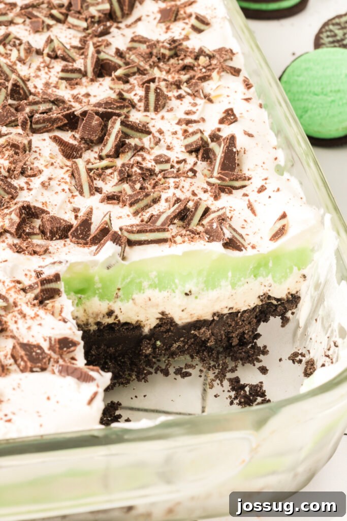 Layers of Luxe: Grasshopper Lasagna 3 A large pan of Grasshopper Lasagna Lush with a piece removed, revealing the beautiful stacked layers of chocolate crust, cream cheese, green mint pudding, and whipped topping.