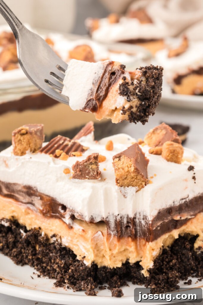 Peanut Butter Cup Dream Lasagna 2 Closeup of a decadent slice of Peanut Butter Cup Lasagna Lush, showcasing its distinct layers of creamy peanut butter, chocolate pudding, and crushed Oreo crust, all topped with whipped cream and mini peanut butter cups.