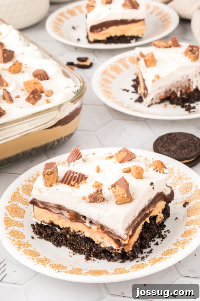 Peanut Butter Cup Dream Lasagna 3 Individual slices of Peanut Butter Cup Lasagna Lush arranged on white plates, highlighting the generous topping of crushed peanut butter cups and whipped cream.