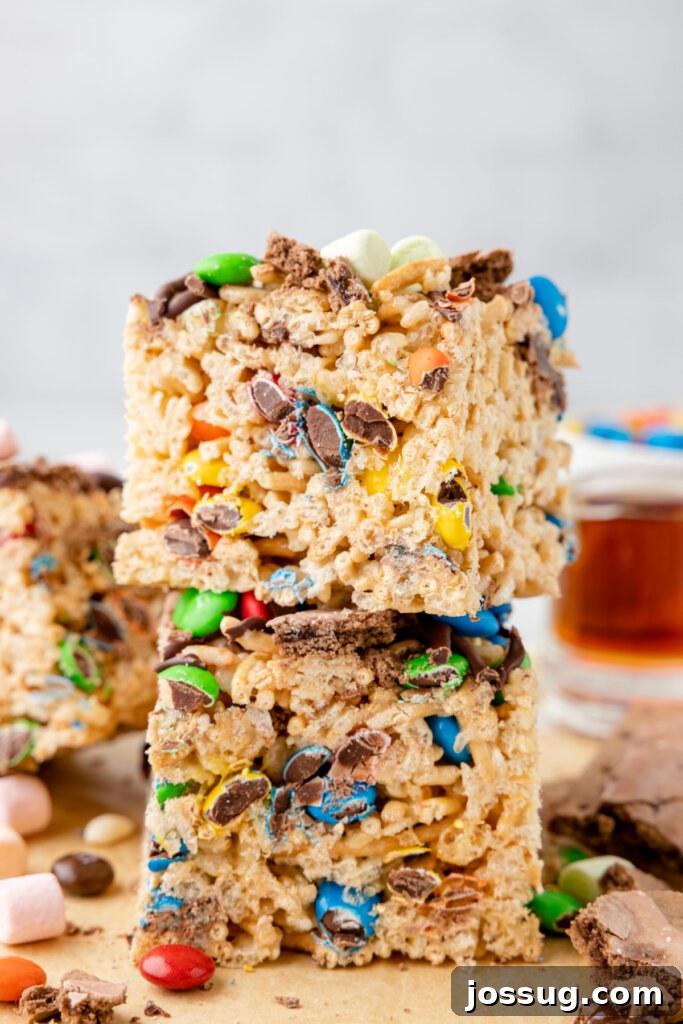 Buddy's Happy Holiday Crispy Treats 5 A festive stack of Buddy the Elf Rice Crispy Treats, garnished with colorful M&M's, chocolate drizzle, and mini marshmallows.