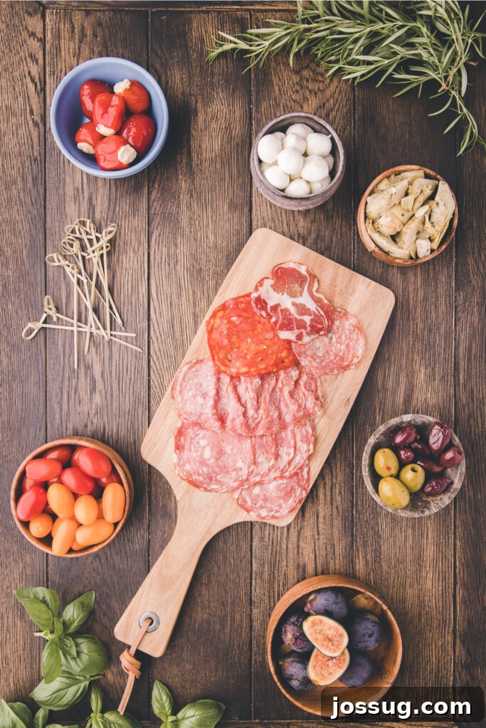 Gourmet Grazing Wreath 3 A vibrant assortment of fresh ingredients including various sliced cured meats, bright red and yellow cherry tomatoes, a medley of olives, and creamy mozzarella pearls, meticulously laid out on a wooden board, awaiting assembly into an Antipasto Wreath.