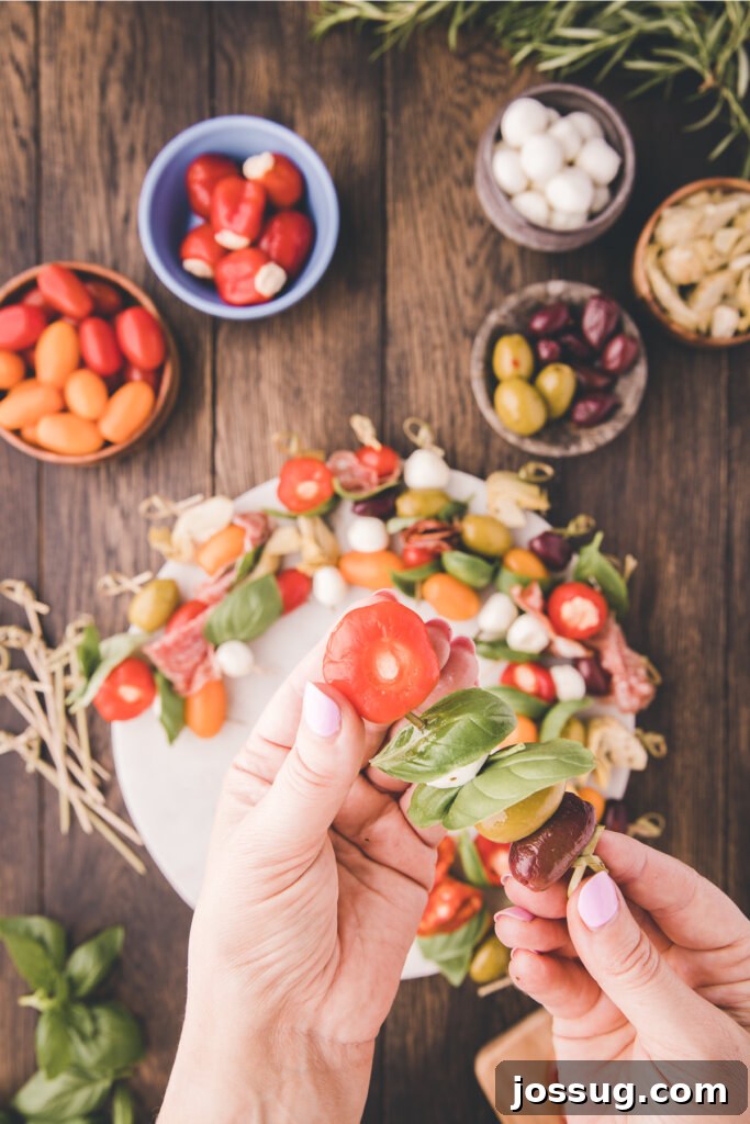 Gourmet Grazing Wreath 4 A hand skillfully threads various vibrant antipasto ingredients onto a bamboo skewer, including a slice of cured meat, a green olive, a white mozzarella pearl, and a bright red cherry tomato, showcasing the careful assembly process.