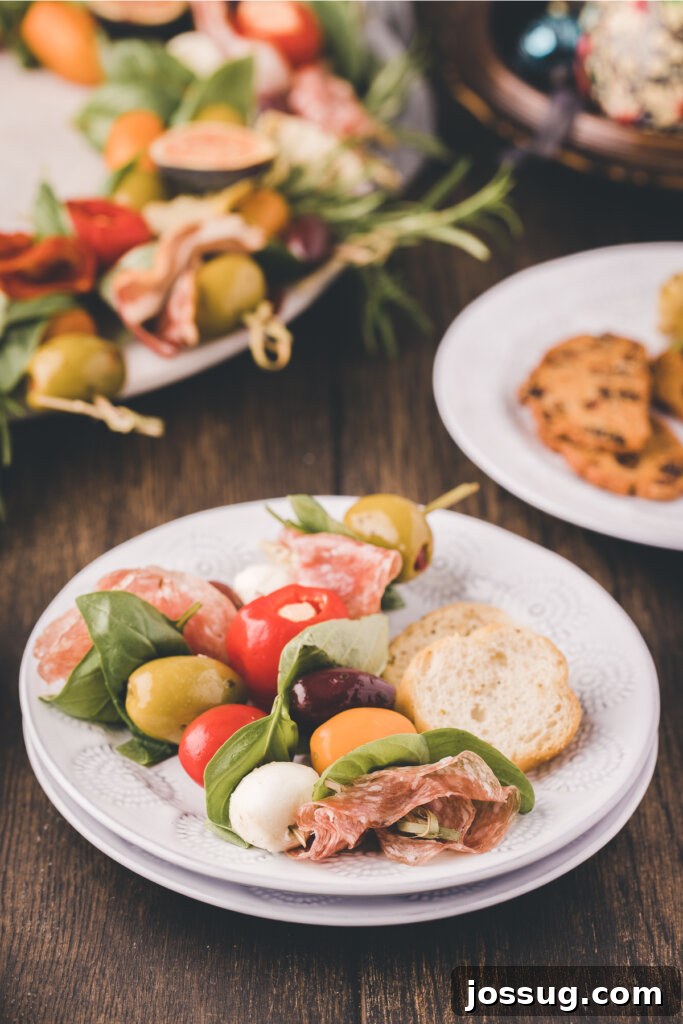 Gourmet Grazing Wreath 9 A single, inviting portion of the Antipasto Wreath, expertly consisting of a skewer laden with an assortment of cured meats, creamy cheese, briny olives, and juicy tomatoes, is elegantly presented on a clean white plate, beckoning guests to indulge.