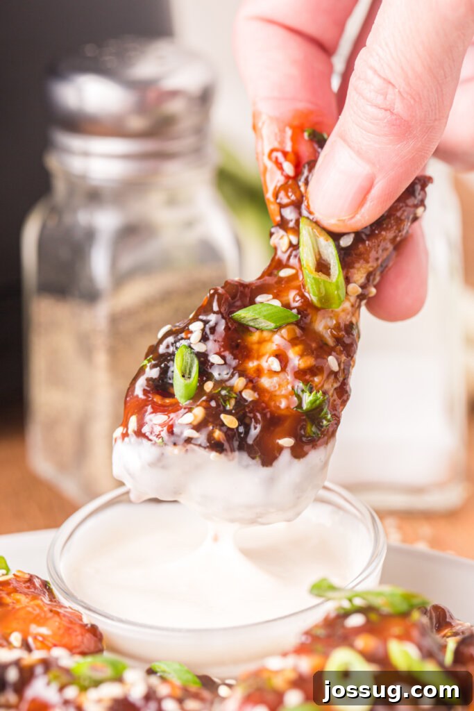 Crispy Sticky Teriyaki Air Fryer Wings 5 hand holding a teriyaki chicken wing dipped into sauce