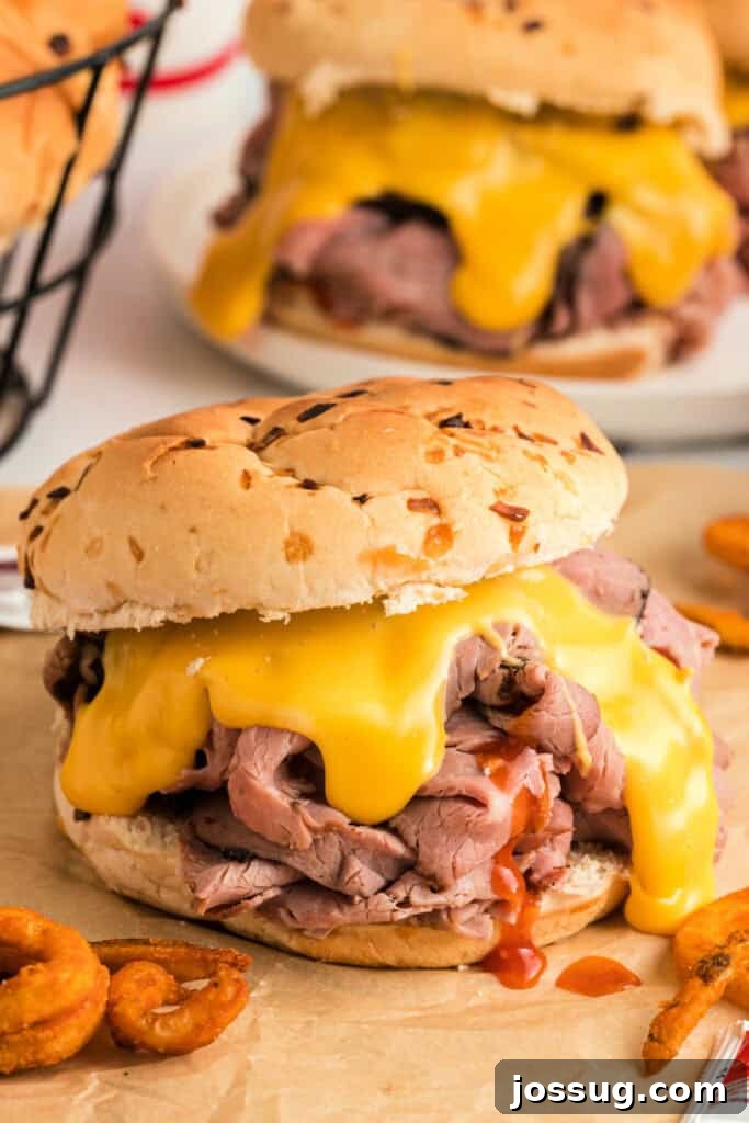 A freshly made copycat Arby's Beef and Cheddar sandwich, golden brown bun, with sauce dripping slightly, ready to be eaten on a clean serving plate.