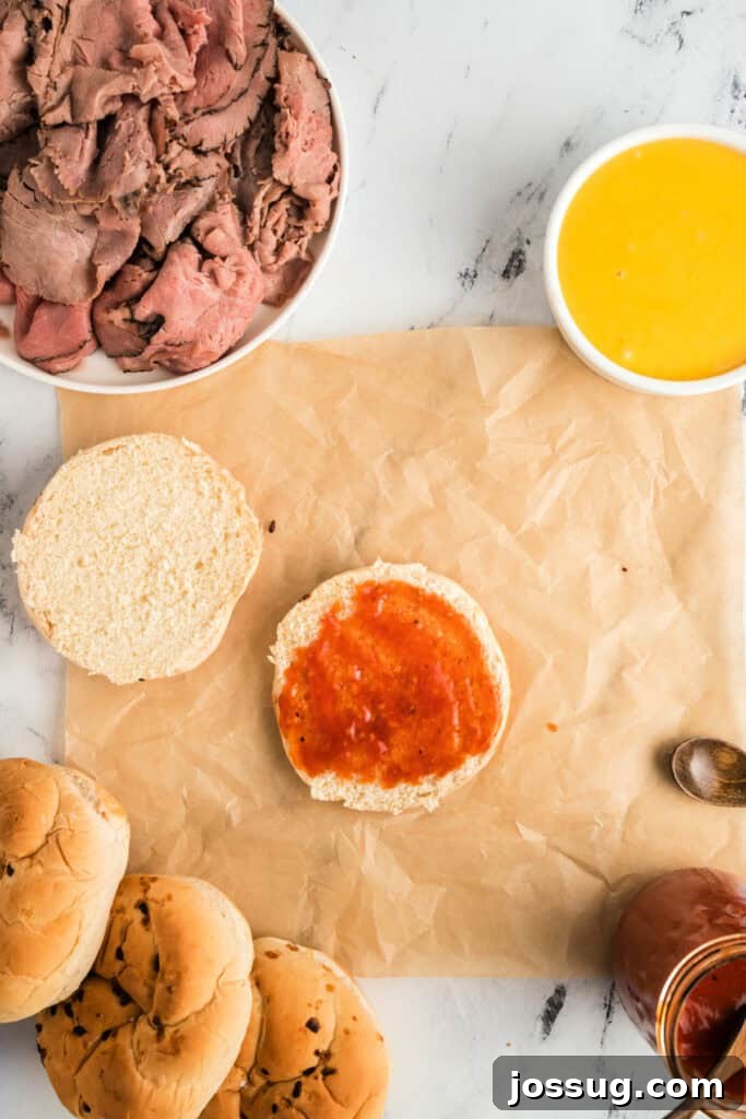 Spreading a generous layer of Arby's sauce onto the bottom half of a sliced Kaiser roll.