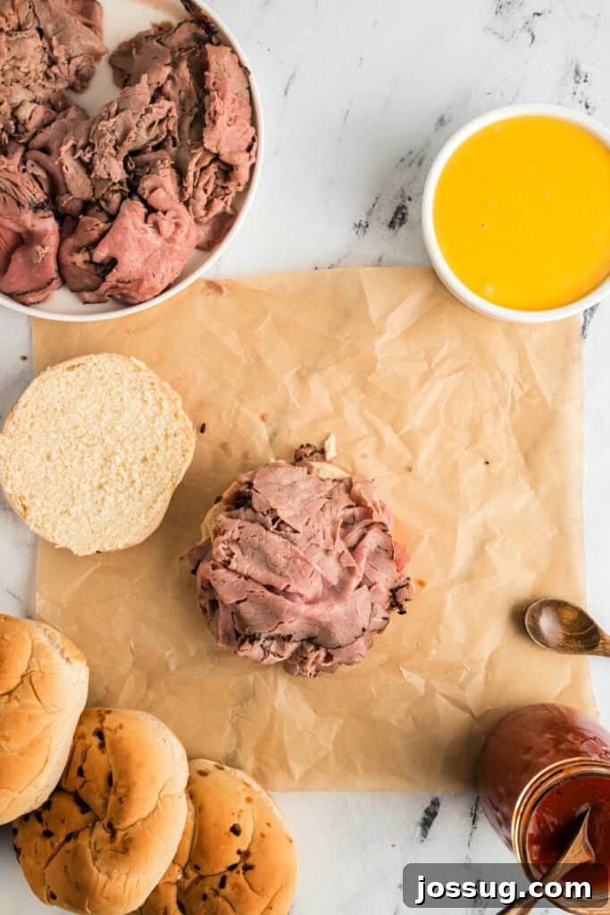 Piling a generous portion of warm, thinly sliced roast beef onto the bottom bun coated with Arby's sauce.