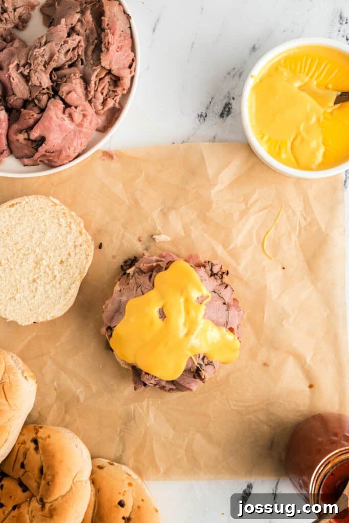 Drizzling a thick layer of creamy cheddar cheese sauce over the piled roast beef on the sandwich bun.