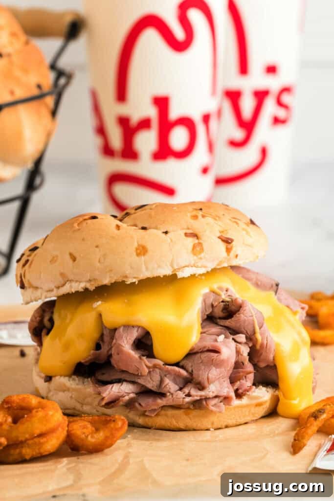 Two copycat Arby's Beef and Cheddar sandwiches on brown paper, with Arby's themed beverage cups blurred in the background, creating a full fast-food experience at home.