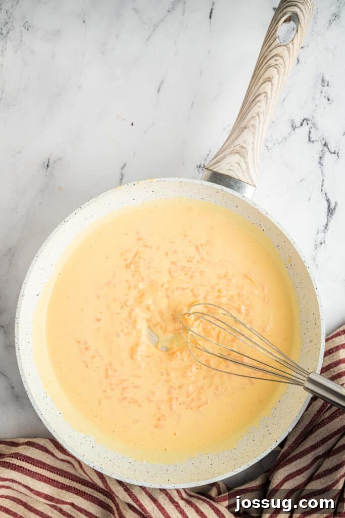 Heating heavy cream and shredded cheddar cheese over medium-low heat, stirring constantly until the cheese melts into a smooth sauce.