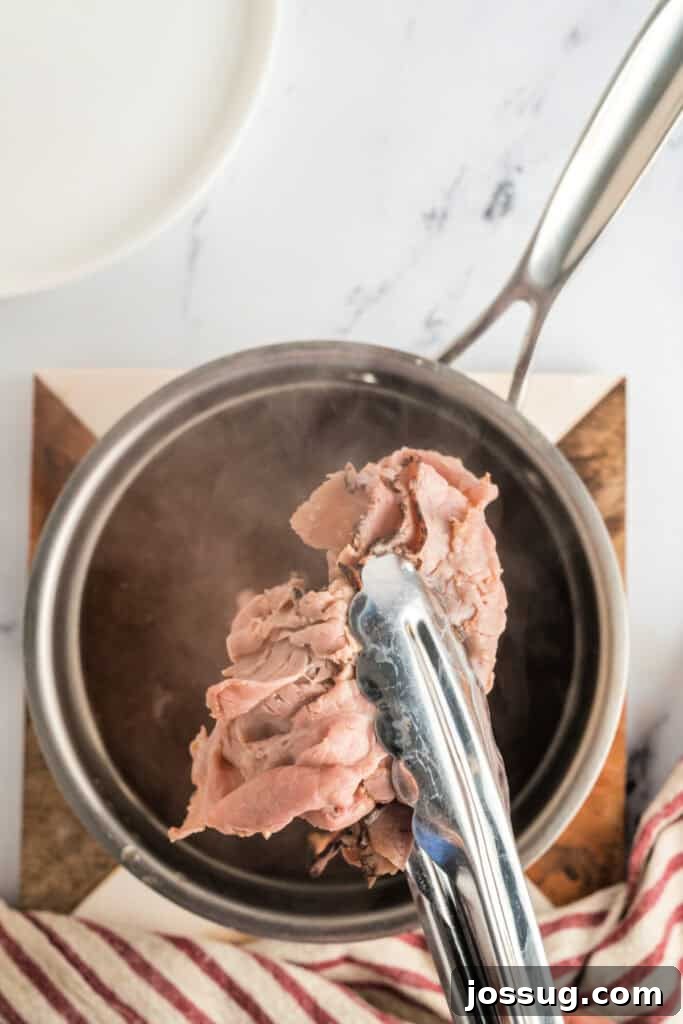 Adding thinly sliced deli roast beef to the warm beef stock, using tongs to immerse pieces.