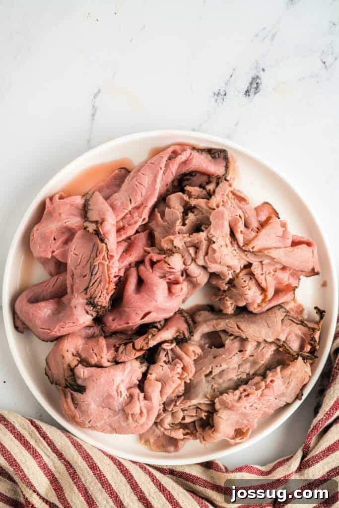 Removing warm roast beef from beef stock with tongs and transferring it to a plate.