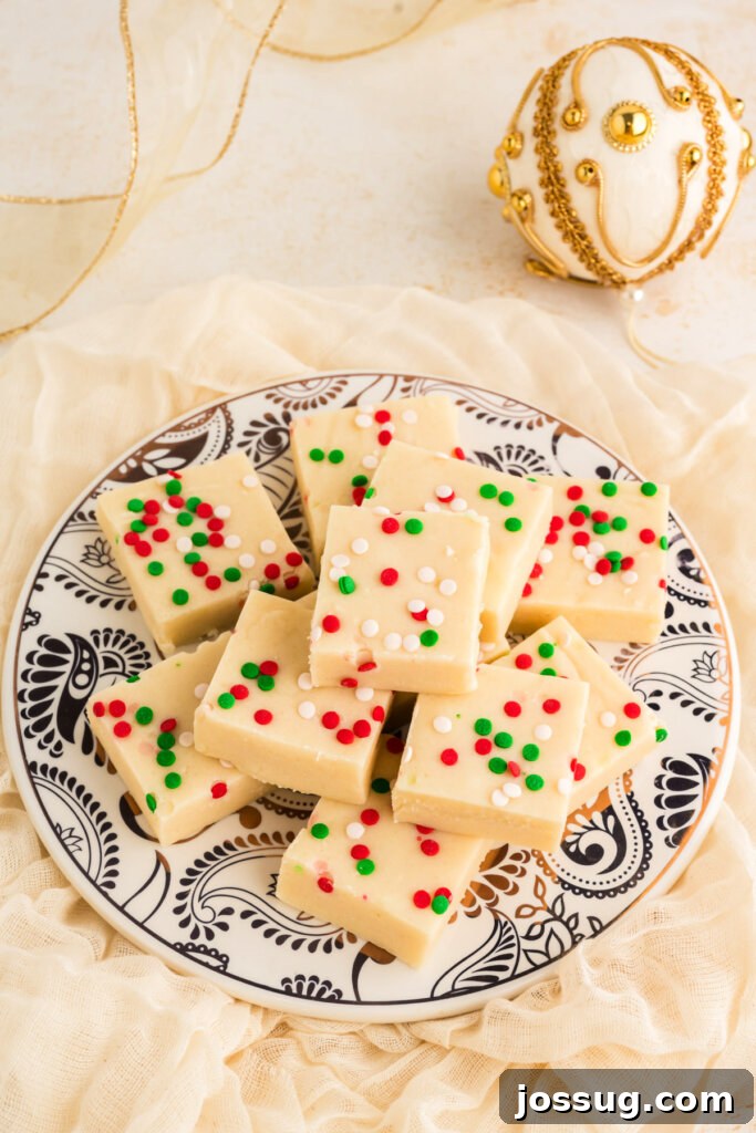 Frosted Sugar Cookie Fudge 3 Close-up of elegantly arranged sugar cookie fudge squares on a festive blue and white ceramic plate, decorated with holiday motifs