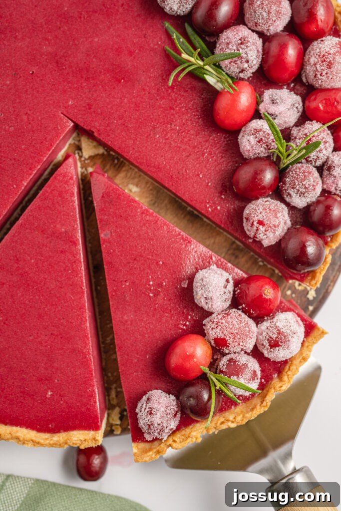 a slice of cranberry tart being removed from the whole pie, showing the vibrant curd