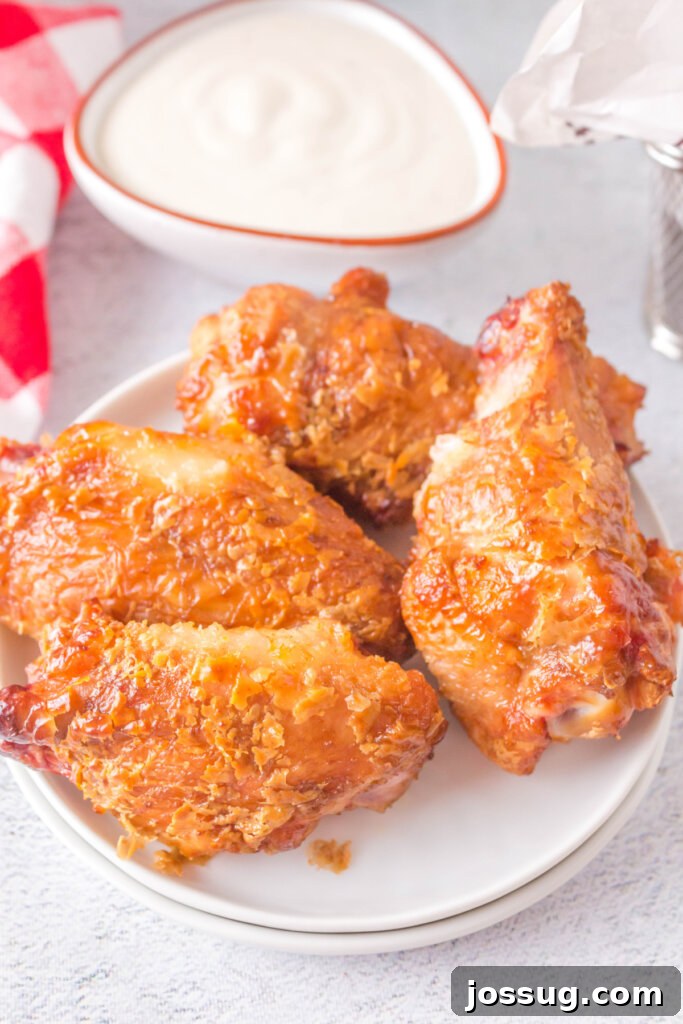 Four perfectly grilled crispy chicken wings arranged on a plate next to a small bowl of dipping sauce, showcasing their golden-brown, inviting texture.