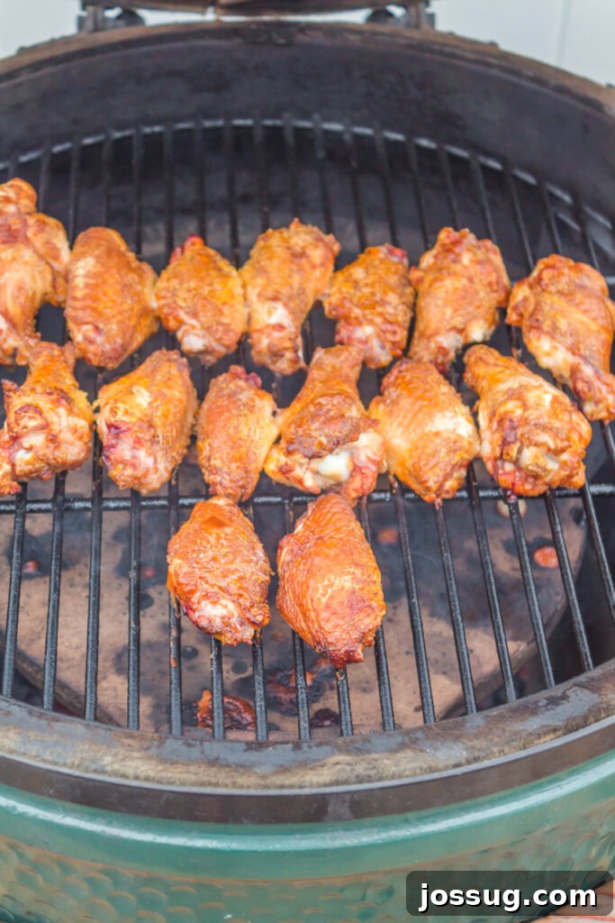 A close-up view of seasoned chicken wings sizzling and charring slightly on the hot grates of a grill, indicating the cooking process.