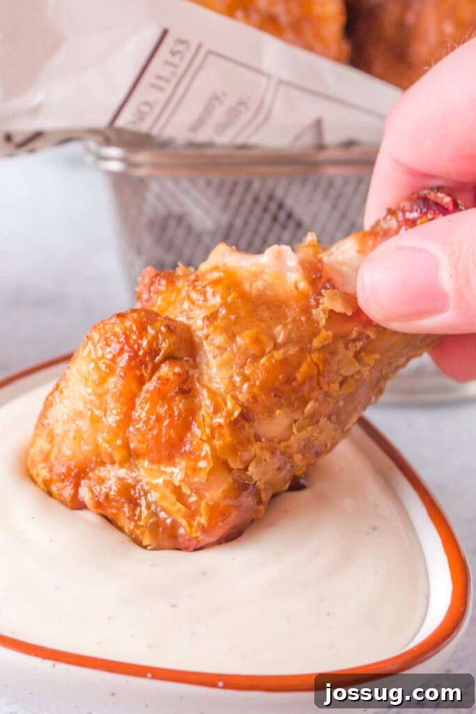 A hand holding a perfectly grilled crispy chicken wing, dipping it into a bowl of rich BBQ sauce, highlighting its saucy potential.