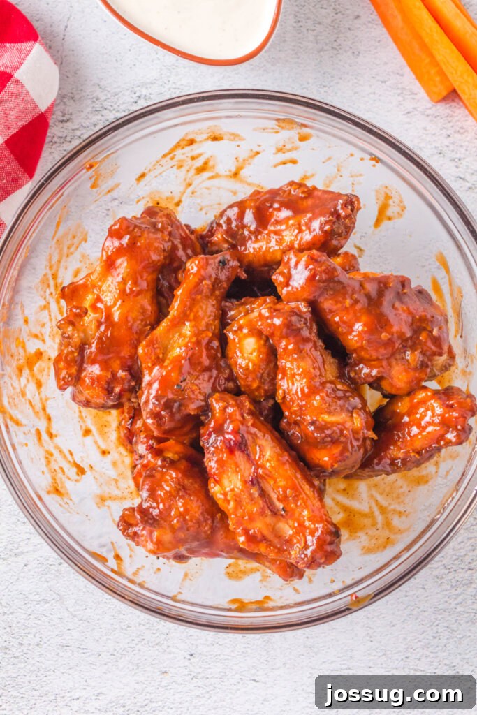 A large bowl filled with grilled crispy chicken wings being generously coated with rich BBQ sauce, ready for serving.