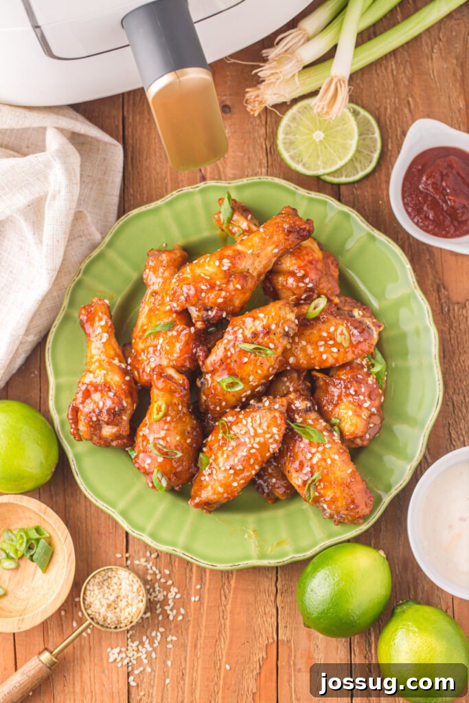 Sticky Honey Sriracha Wings 2 Looking down onto vibrant honey sriracha wings, garnished with sesame seeds and green onions, served on a stylish green plate, showcasing their irresistible glaze.