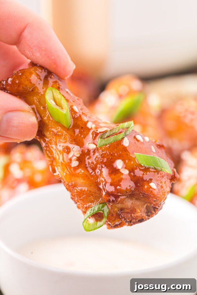 Sticky Honey Sriracha Wings 5 A hand reaching to dip a perfectly glazed honey sriracha wing into a small bowl of extra sauce, highlighting its deliciousness and the option for dipping.