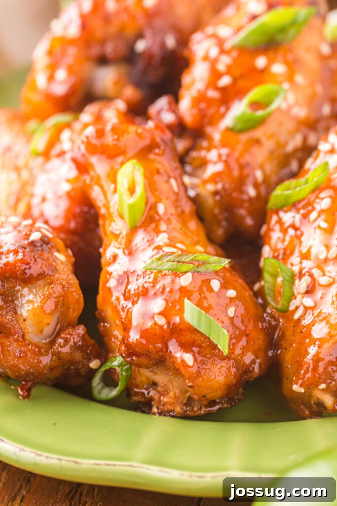 Sticky Honey Sriracha Wings 6 A very close-up shot of a single honey sriracha wing, showing its glistening glaze, crispy skin, and sesame seed garnish in detail.