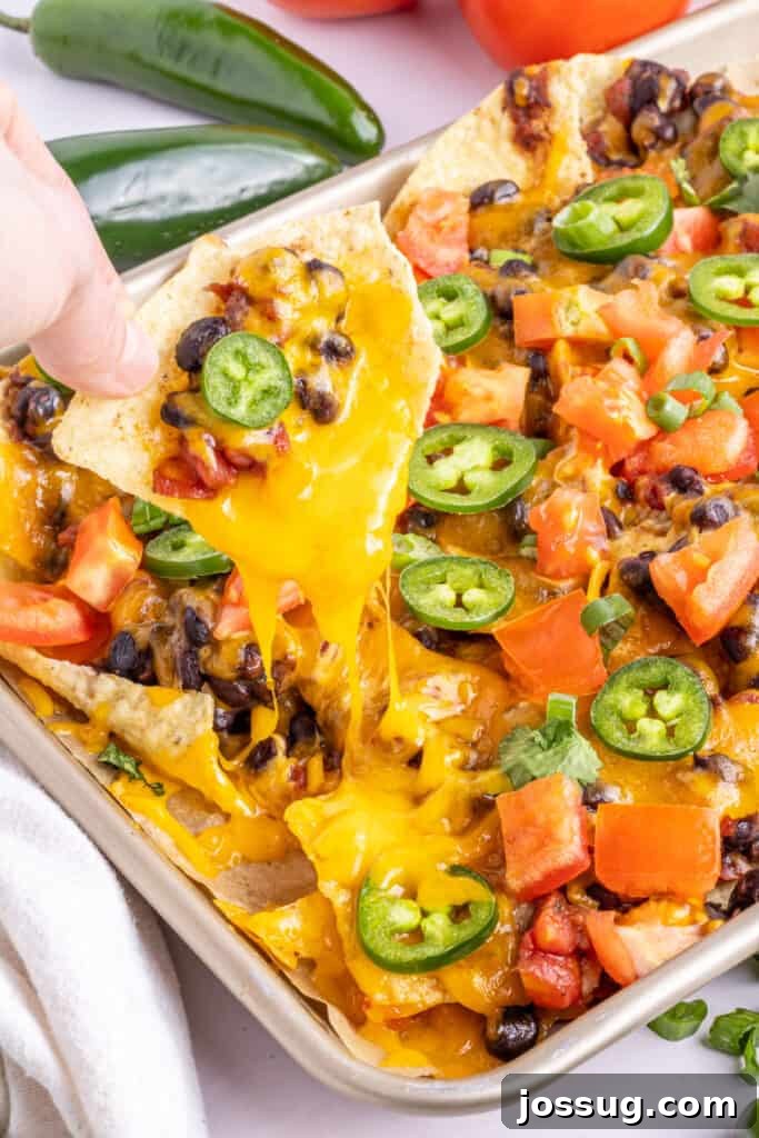 Volcano Black Bean Nachos 5 A hand reaching to pull a perfectly loaded spicy black bean nacho from a sheet pan, showing its enticing gooey cheese pull.